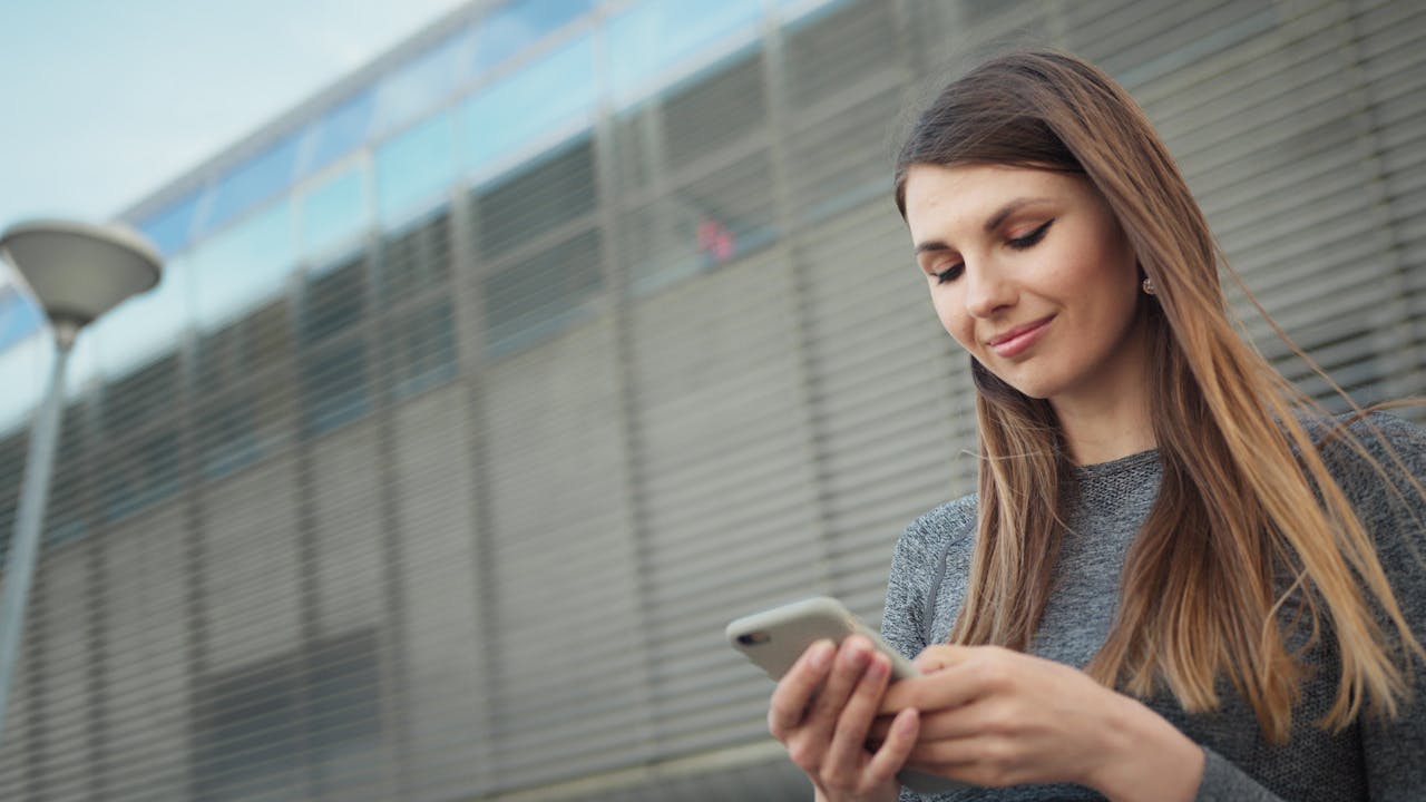 Young woman smiling while using a smartphone outside in an urban area.