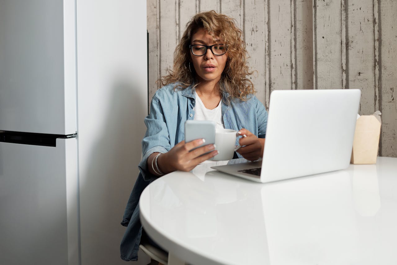 A woman engages in remote work, using a smartphone and laptop at home.