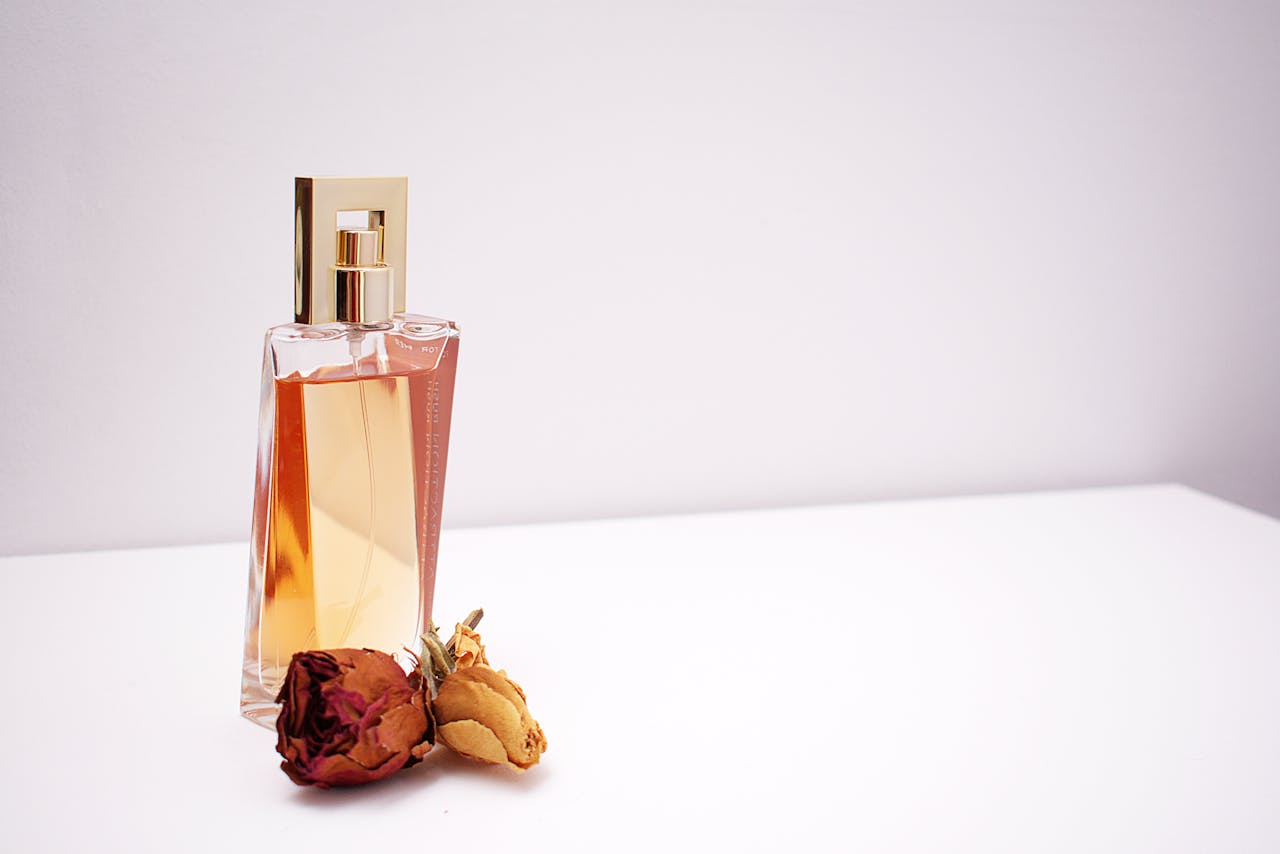 services-04 Elegant glass perfume bottle with luxurious design placed next to dried flowers against a minimalistic white background.