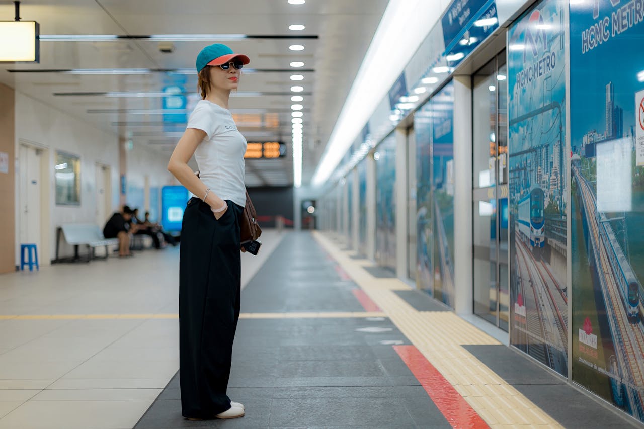 services-01 Woman standing alone at HCMC Metro station, dressed casually with sunglasses and cap.