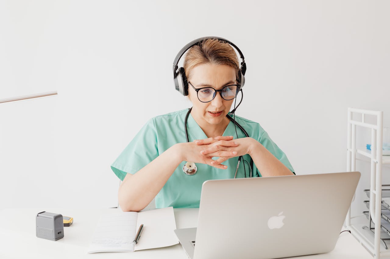 Doctor in scrubs having an online video call from her office, wearing headphones.