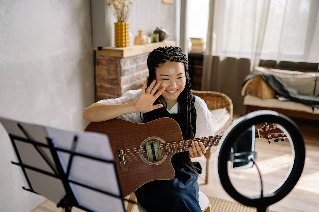 Smiling woman streaming acoustic guitar session from home using smartphone and ring light.