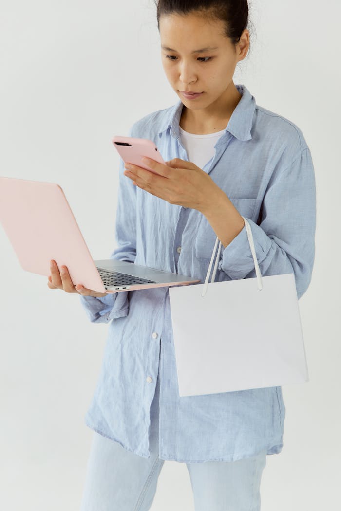 Woman in casual attire shopping online using a laptop and phone indoors.